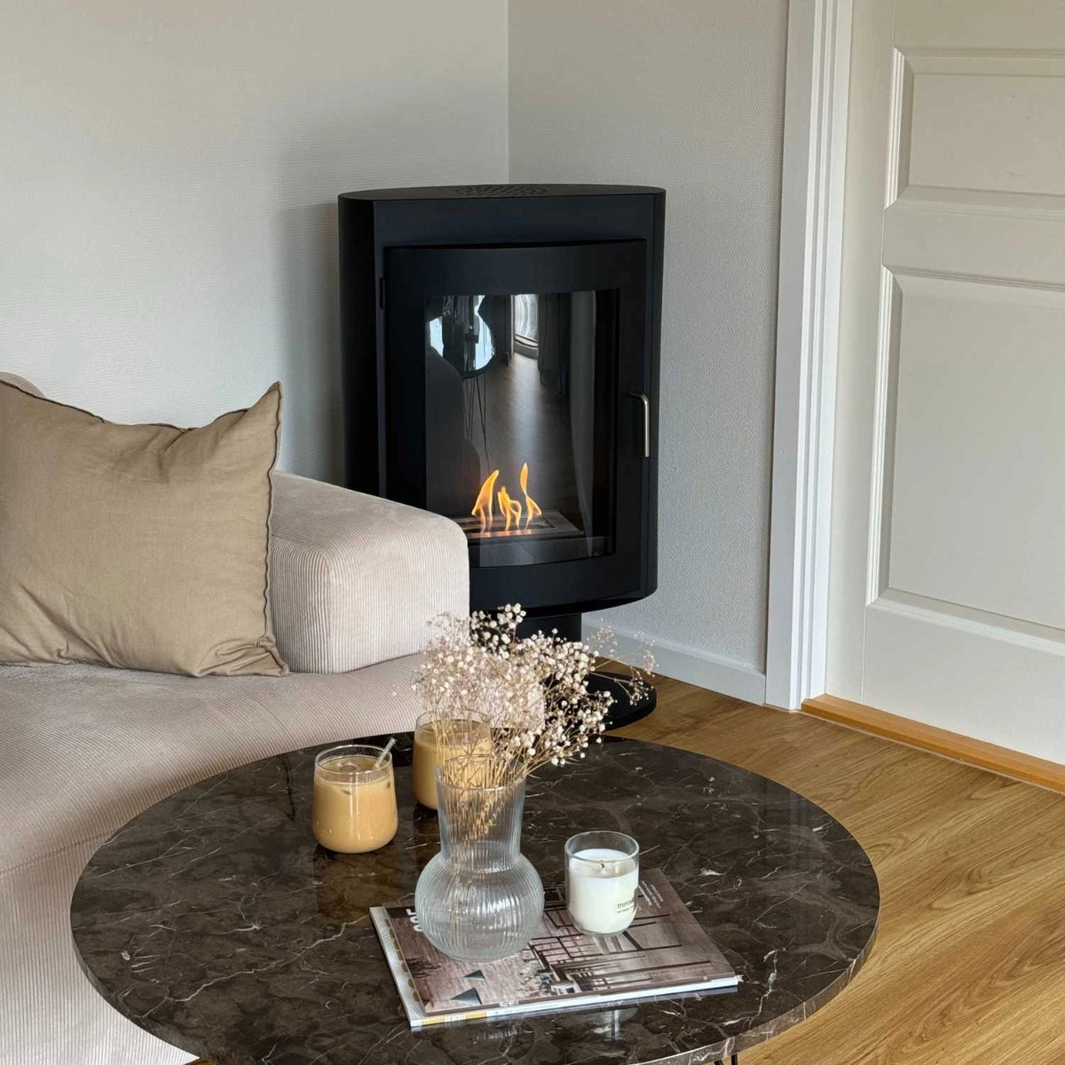 Trenton bioethanol stove fireplace in a living room corner, lit flame, with a styled marble coffee table
