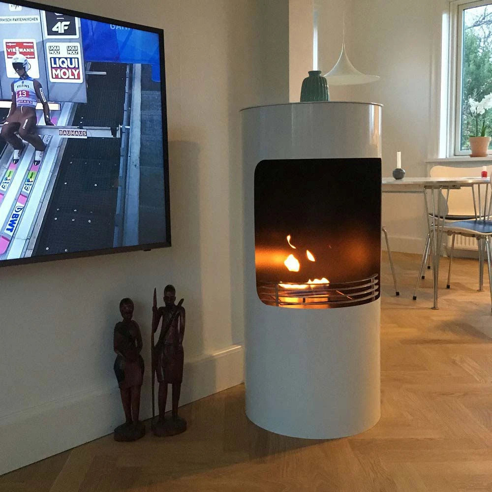 Montgomery white bioethanol fireplace lit in a living room with wall-mounted TV and decorative statues