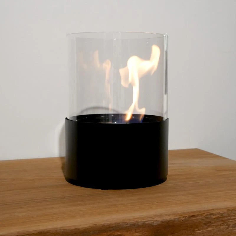 Close-up of the Kennington fireplace's lit flame inside the glass cylinder, on a wooden table