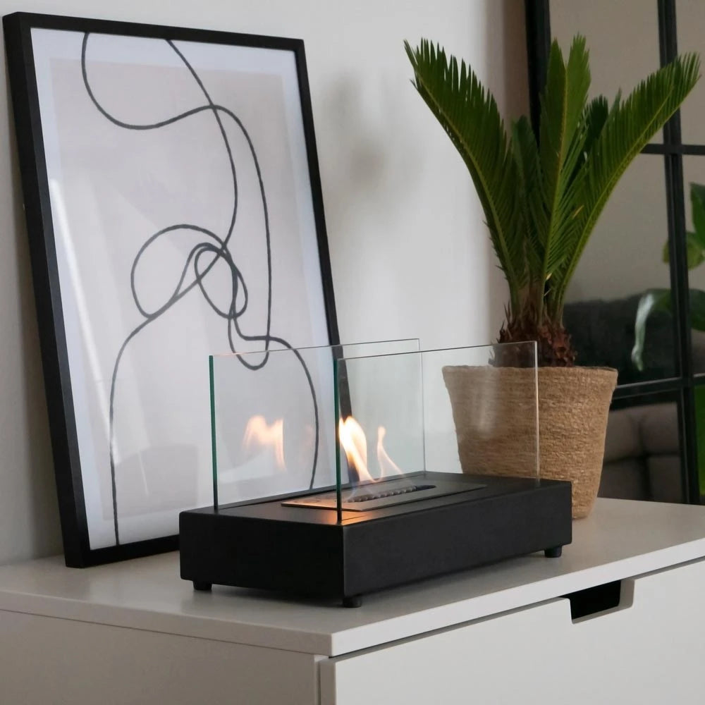 Lambeth black bioethanol fireplace lit on a white sideboard beside a plant and framed art