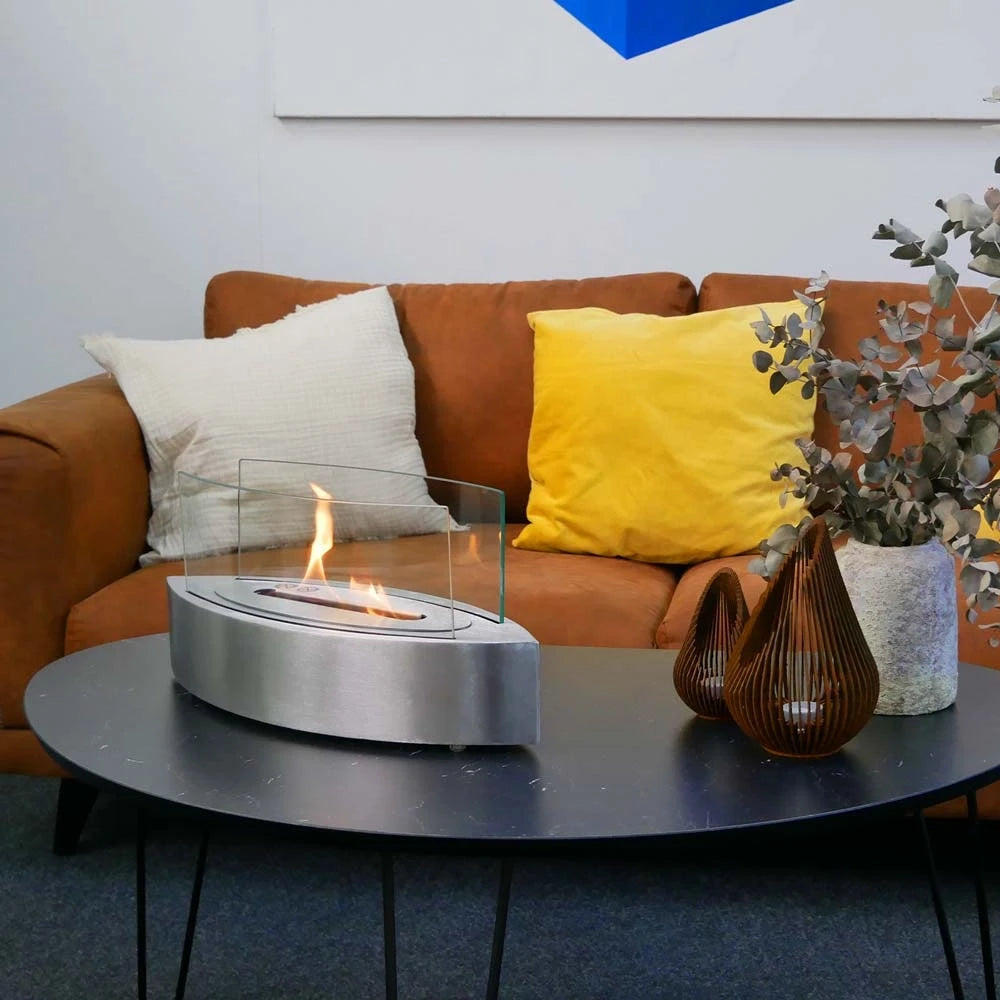 ScandiFlames oval steel tabletop bioethanol fireplace lit on a coffee table beside an orange sofa