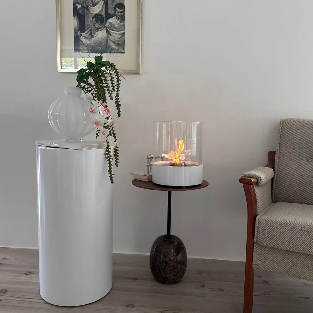 ScandiFlames Dualis White 2-in-1 bioethanol fireplace: the floor-standing base styled as a pedestal with a vase, and the burner and glass lifted out for lit tabletop use on a side table beside an armchair
