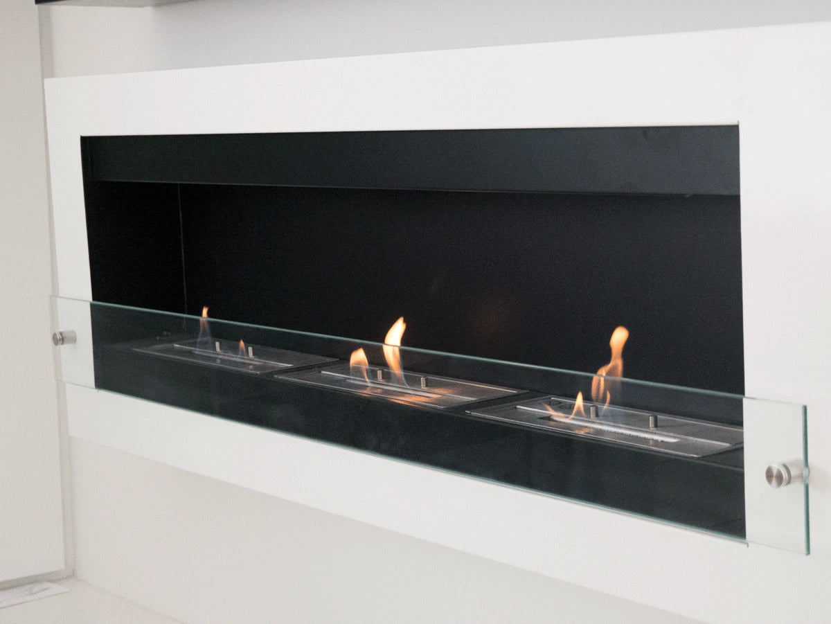 XL white wall-mounted bioethanol fireplace recessed into a white wall with three lit ethanol flames behind the safety glass