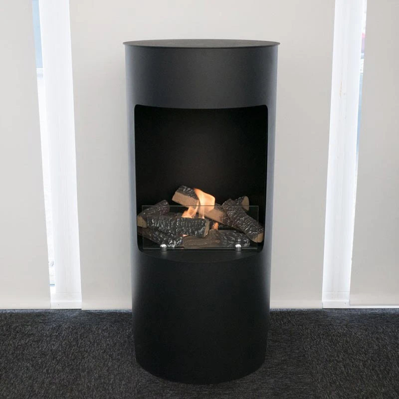 Montgomery black bioethanol fireplace with decorative logs, lit, against a light grey wall on dark flooring