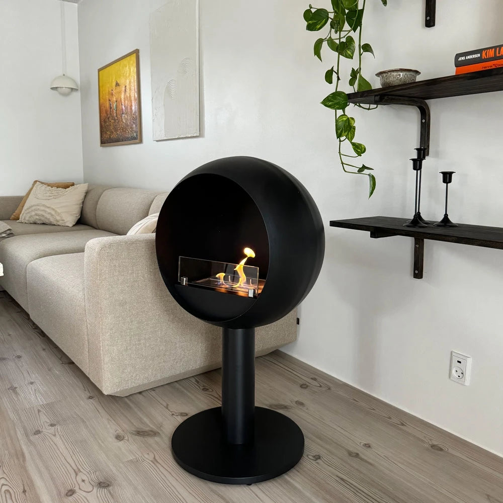 Edmonton freestanding bioethanol fireplace lit beside a sofa with wall shelving in a living room