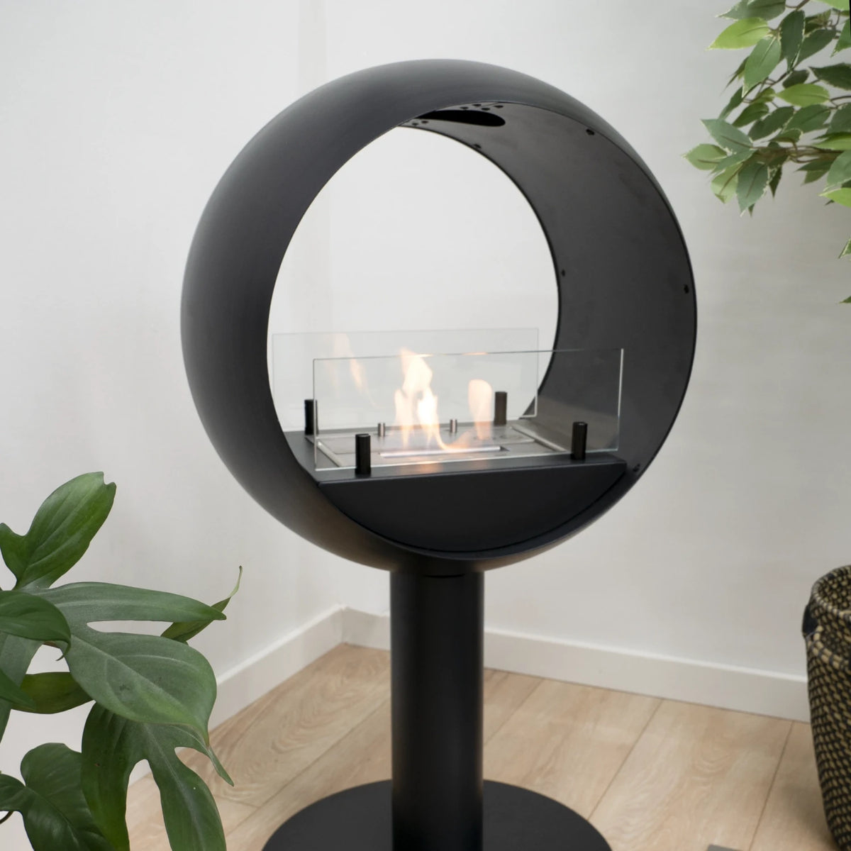 Edmonton 2-sided freestanding bioethanol fireplace lit in a living room with houseplants and a wicker basket