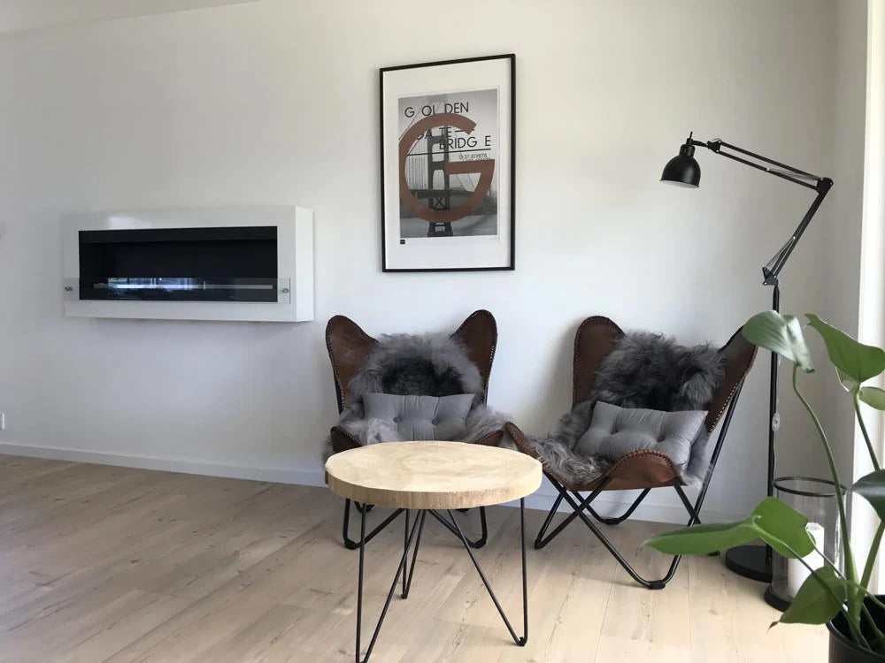 Wide view of the XL wall-mounted white bioethanol fireplace, unlit, in a living room with wingback chairs and a floor lamp