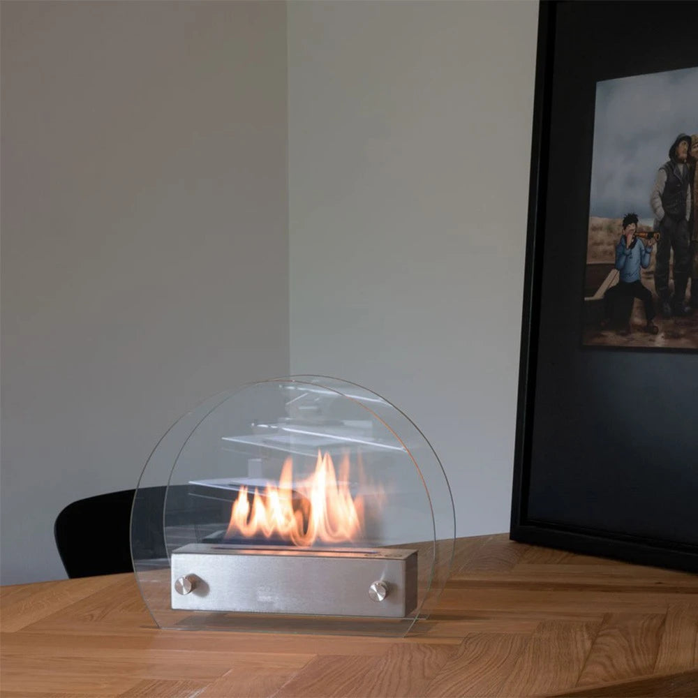 Circular table bioethanol fireplace lit on a wooden dining table with a framed art print in the background