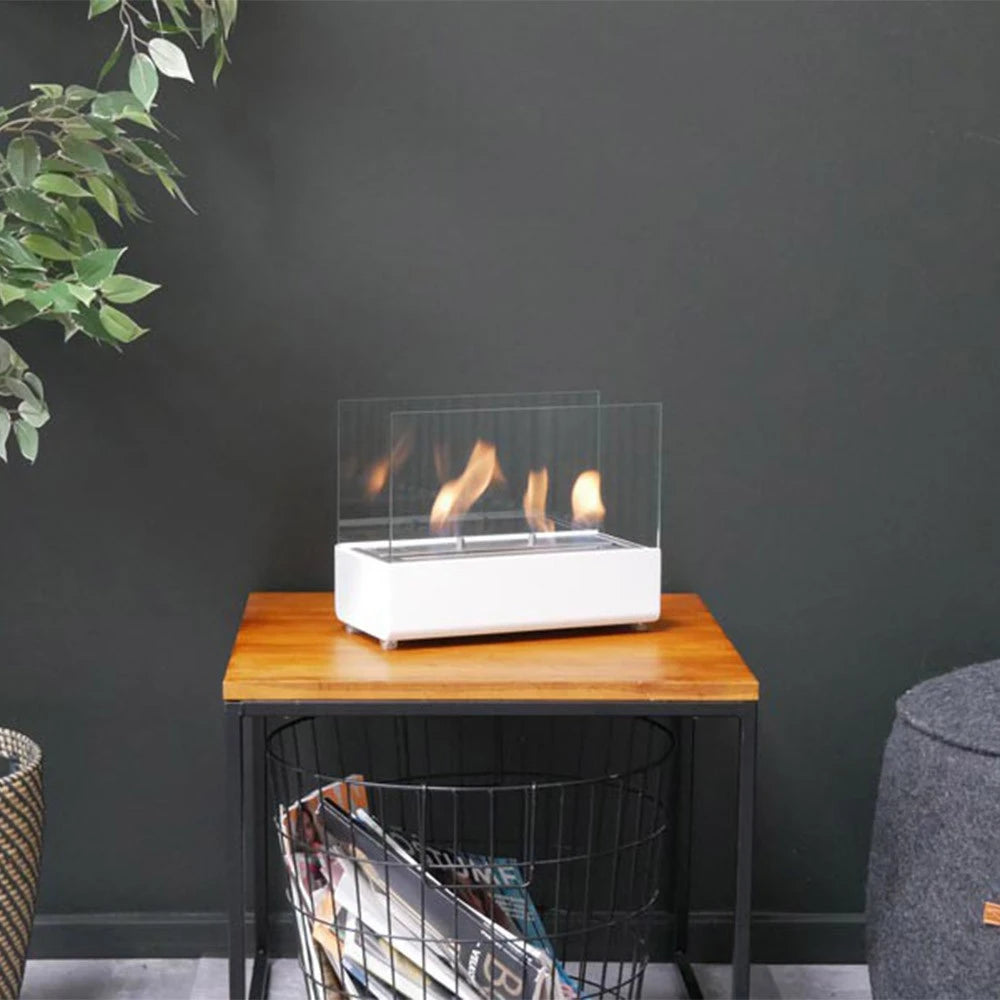 ScandiFlames white tabletop bioethanol fireplace lit on a wooden side table beside a plant and magazine basket