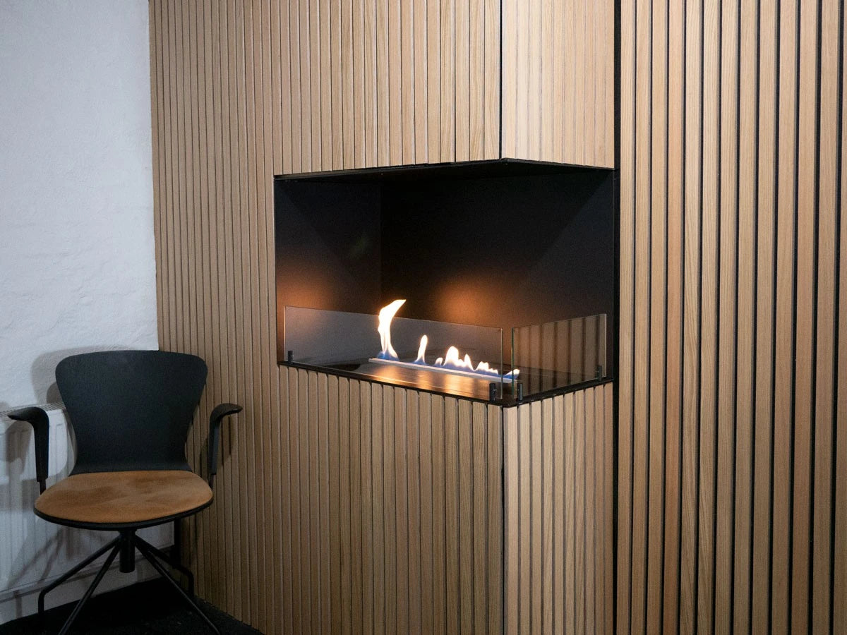 Foco Corner Right 800 built into a light oak wood-slat corner wall, with a realistic lit ethanol flame, in a showroom setting.
