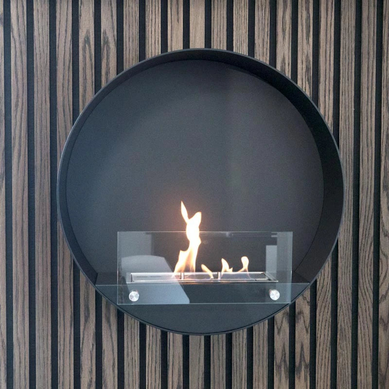 Delaware black round bio fireplace mounted on a slatted wood-panelled wall, lit flame