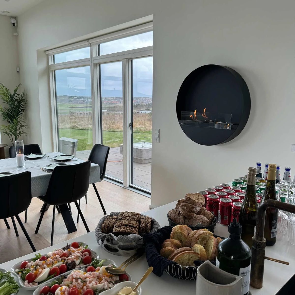 Delaware XL black round bio fireplace mounted in a dining room during a gathering, lit with a realistic flame