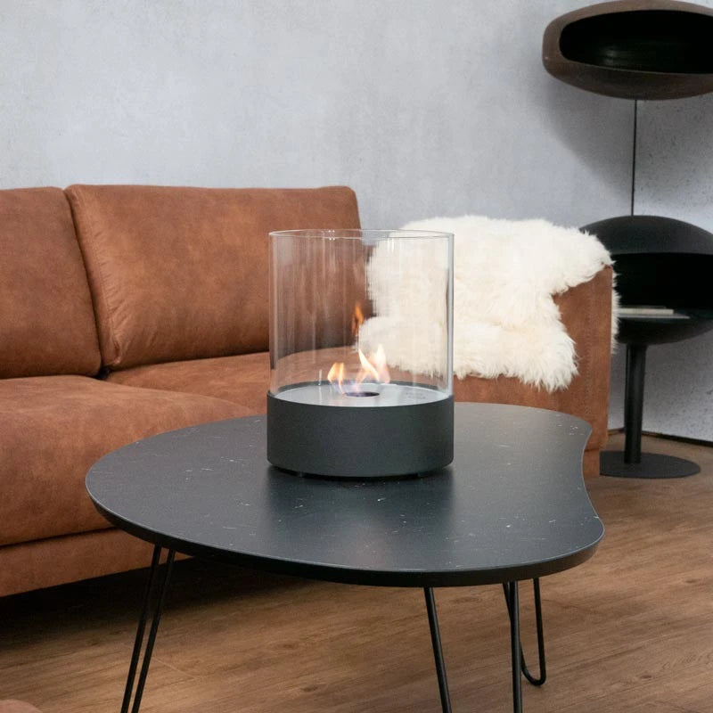 Southwark black round tabletop bioethanol fireplace on a black coffee table with a tan sofa and sheepskin throw, lit flame