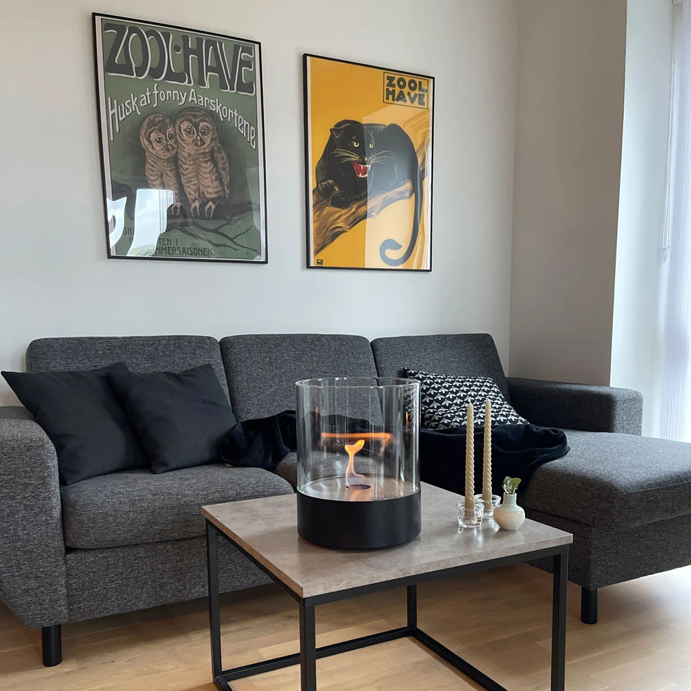 Southwark black round tabletop bioethanol fireplace on a coffee table with a grey sofa and candles, lit flame