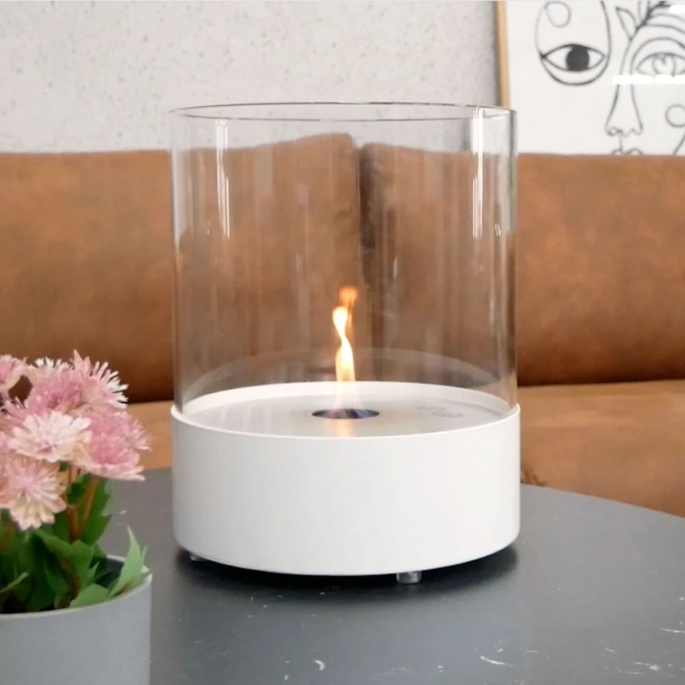 Southwark white round tabletop bioethanol fireplace, lit flame, on a coffee table with a sofa and pink flowers
